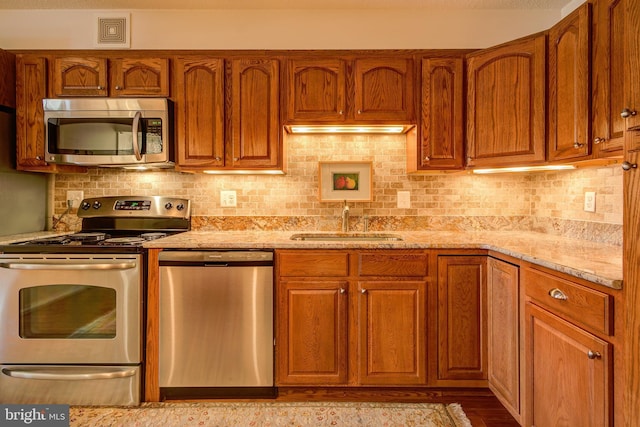 kitchen featuring a sink, visible vents, appliances with stainless steel finishes, light stone countertops, and tasteful backsplash