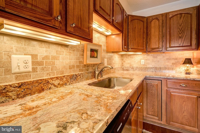 kitchen featuring light stone counters, brown cabinets, a sink, and decorative backsplash