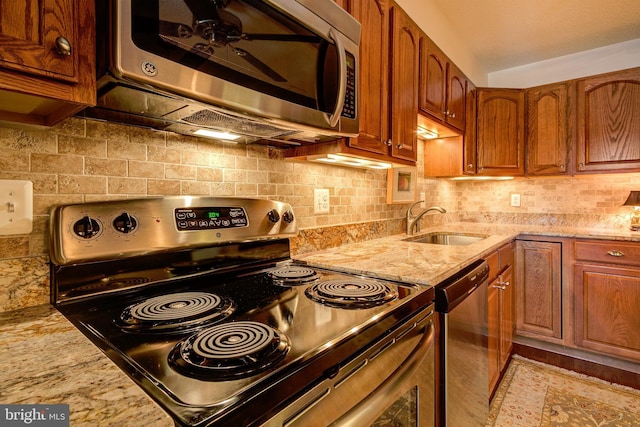 kitchen featuring tasteful backsplash, appliances with stainless steel finishes, brown cabinets, light stone counters, and a sink