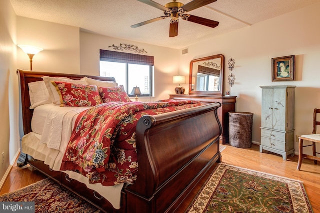 bedroom featuring a ceiling fan, a textured ceiling, baseboards, and wood finished floors