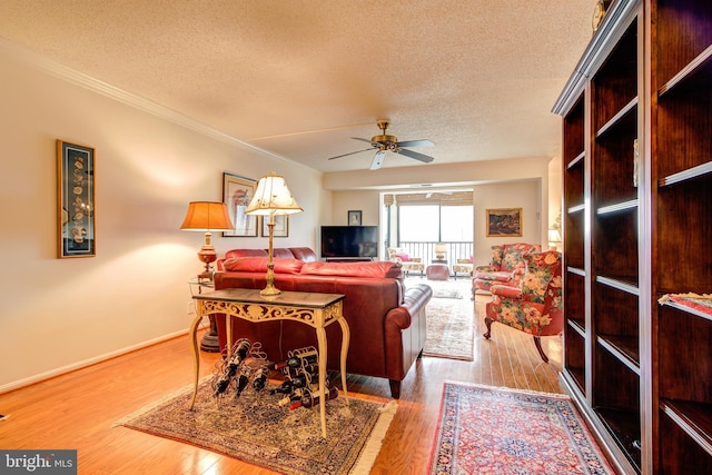 living room with ornamental molding, a ceiling fan, a textured ceiling, wood finished floors, and baseboards