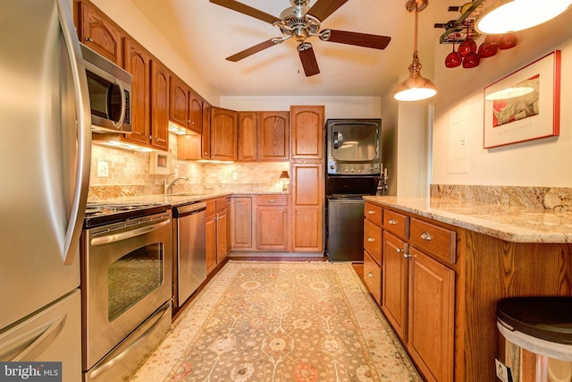 kitchen with stainless steel appliances, light stone counters, backsplash, and stacked washer and clothes dryer