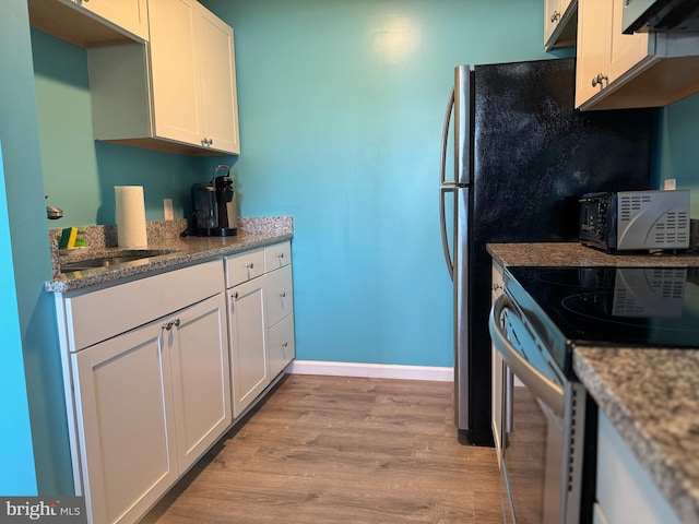 kitchen with stainless steel electric range, white cabinetry, light wood-type flooring, under cabinet range hood, and baseboards