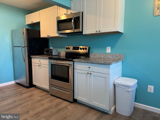 kitchen with stainless steel appliances, white cabinets, baseboards, and wood finished floors