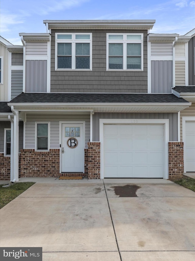 townhome / multi-family property with an attached garage, roof with shingles, concrete driveway, and brick siding