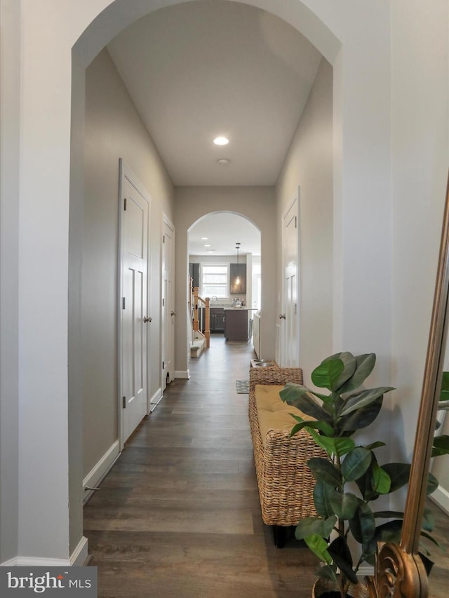 corridor featuring dark wood-style floors, arched walkways, and baseboards