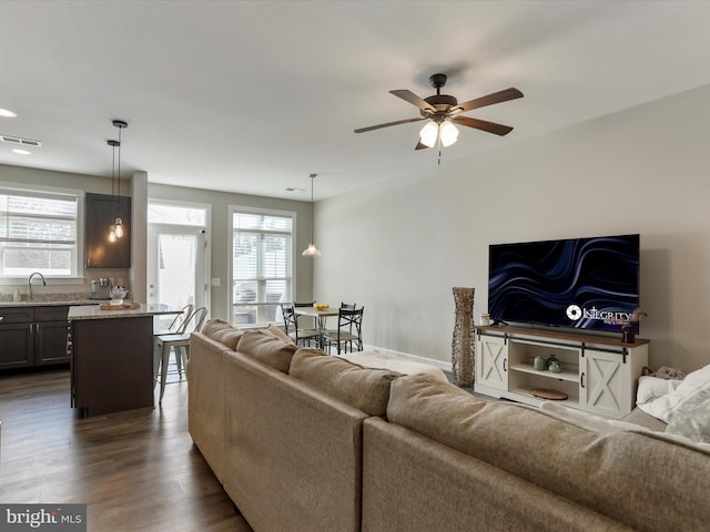 living area featuring plenty of natural light, visible vents, ceiling fan, and dark wood-style flooring