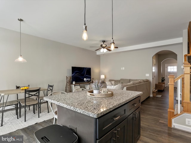 kitchen with dark wood-style floors, arched walkways, open floor plan, a kitchen island, and light stone countertops