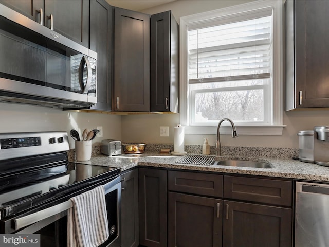 kitchen with light stone countertops, dark brown cabinetry, stainless steel appliances, and a sink