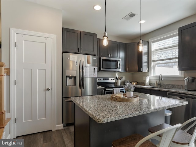 kitchen featuring light stone counters, pendant lighting, appliances with stainless steel finishes, dark brown cabinetry, and a sink