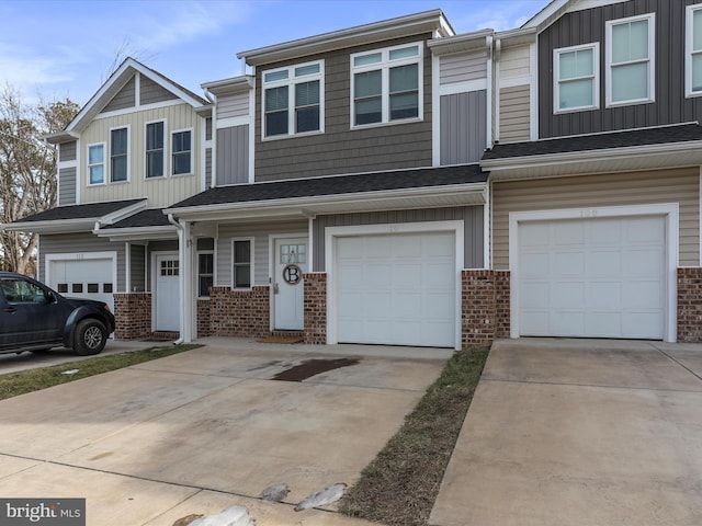 view of property featuring an attached garage, driveway, a shingled roof, and brick siding