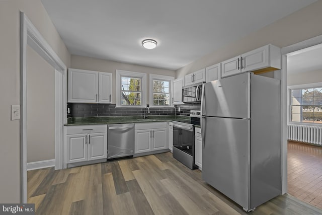 kitchen with dark countertops, light wood-style flooring, appliances with stainless steel finishes, and white cabinets