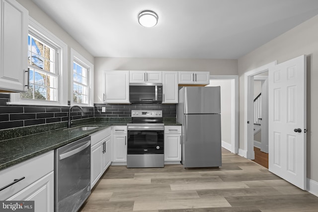 kitchen featuring stainless steel appliances, white cabinets, a sink, and backsplash