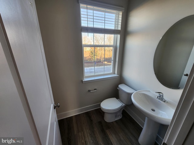 half bathroom with a wealth of natural light, baseboards, toilet, and wood finished floors