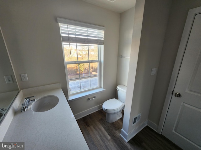 half bath with toilet, wood finished floors, visible vents, vanity, and baseboards