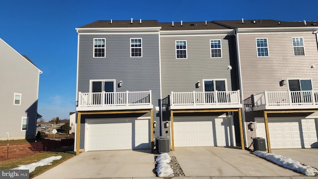 back of house with an attached garage, a balcony, central AC, and concrete driveway