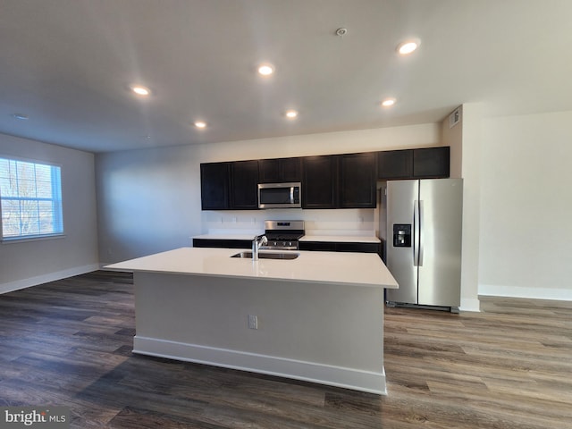 kitchen with dark wood-type flooring, a center island with sink, stainless steel appliances, and light countertops