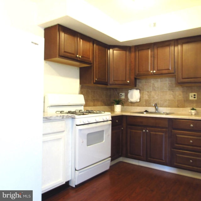 kitchen with white appliances, a sink, light countertops, decorative backsplash, and dark wood-style floors