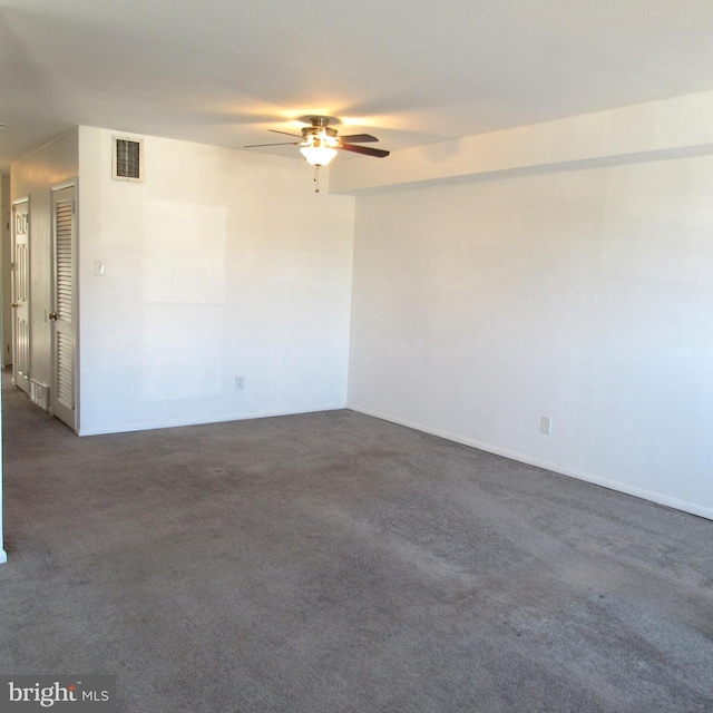 empty room featuring dark carpet, visible vents, and ceiling fan