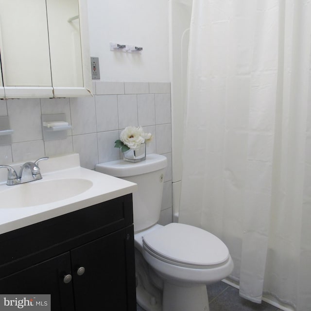 bathroom with toilet, curtained shower, tile patterned flooring, vanity, and tile walls