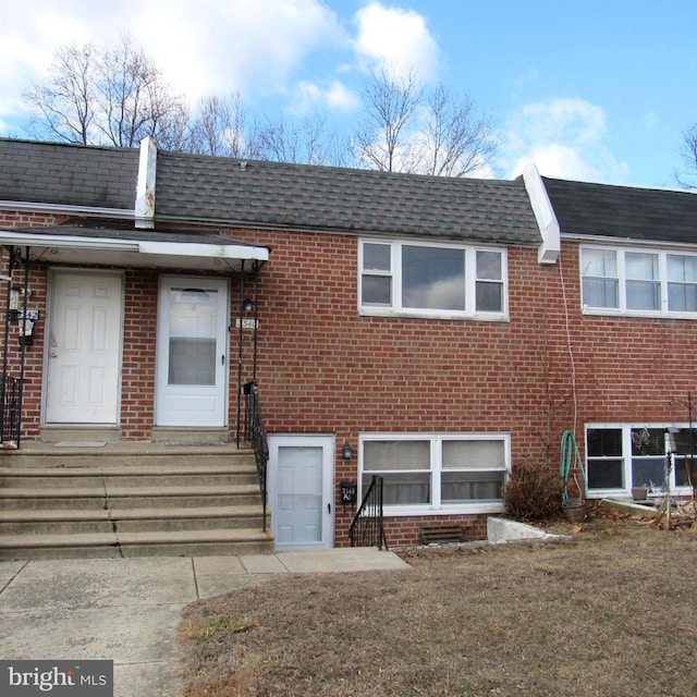 view of front of home featuring brick siding, roof with shingles, mansard roof, entry steps, and a front lawn