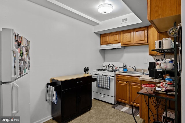 kitchen with white appliances, brown cabinetry, light countertops, under cabinet range hood, and a sink