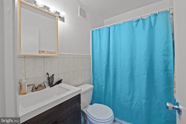 bathroom with visible vents, a shower with shower curtain, toilet, vanity, and tile walls