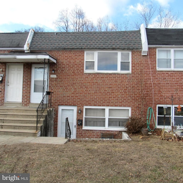 view of front of home featuring a shingled roof, entry steps, brick siding, and a front yard