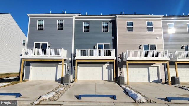 rear view of house featuring central air condition unit, a balcony, an attached garage, and driveway