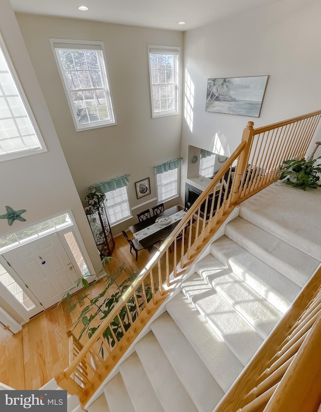 staircase featuring wood finished floors, a towering ceiling, and recessed lighting