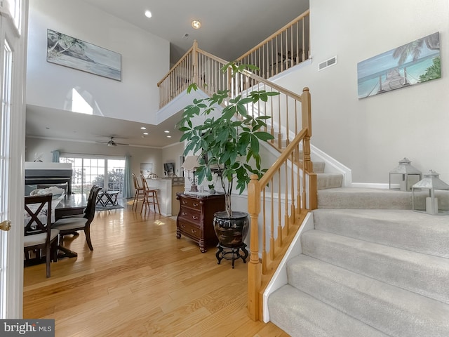 staircase with a high ceiling, wood finished floors, visible vents, and recessed lighting