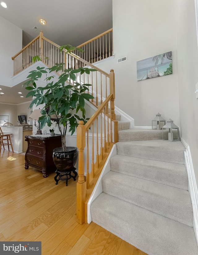 stairs featuring recessed lighting, visible vents, a high ceiling, and wood finished floors