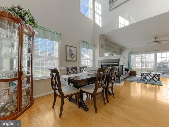 dining area featuring baseboards, ceiling fan, ornamental molding, light wood-style floors, and a multi sided fireplace