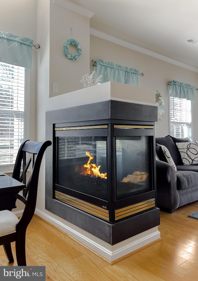 room details featuring wood finished floors, a multi sided fireplace, visible vents, and crown molding