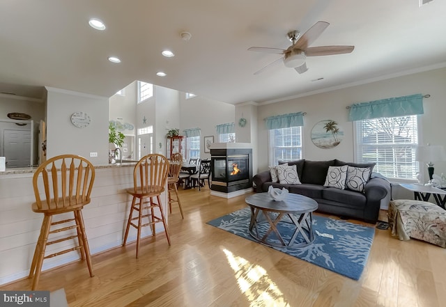 living room with light wood finished floors, recessed lighting, ornamental molding, a ceiling fan, and a multi sided fireplace