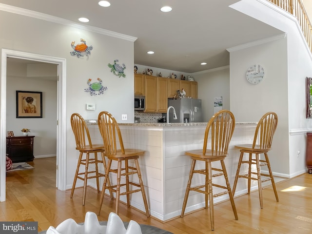 kitchen featuring light brown cabinets, stainless steel appliances, light wood-style floors, a kitchen breakfast bar, and light countertops