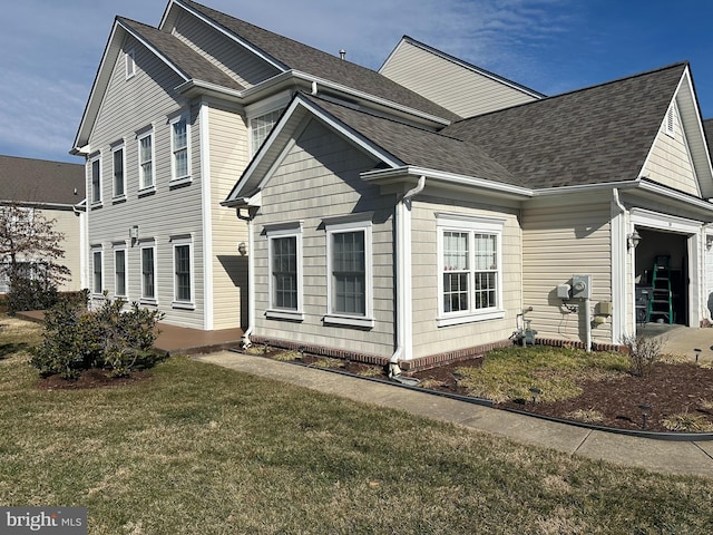 view of front facade with a front yard, roof with shingles, and an attached garage