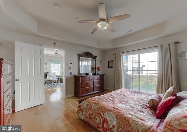 bedroom with light wood-type flooring, a tray ceiling, access to outside, and a ceiling fan