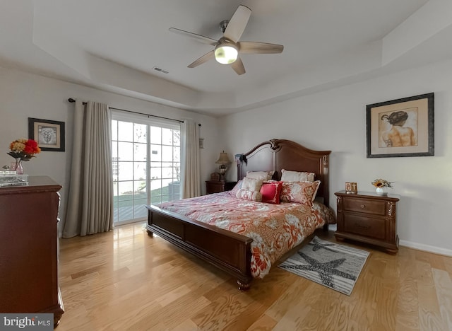 bedroom with visible vents, baseboards, light wood-style flooring, access to outside, and a tray ceiling