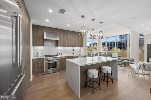 kitchen featuring visible vents, premium appliances, modern cabinets, decorative light fixtures, and under cabinet range hood