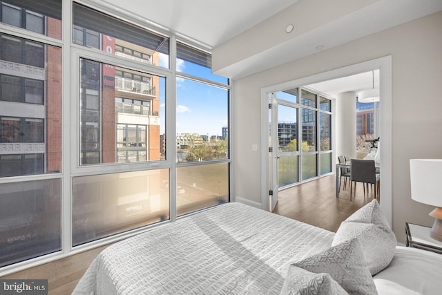 bedroom featuring a view of city, floor to ceiling windows, and wood finished floors