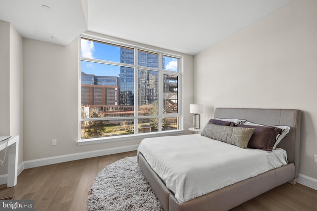 bedroom with light wood-type flooring, a city view, and baseboards