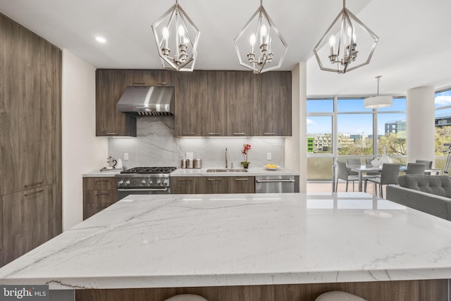 kitchen with stainless steel appliances, a sink, wall chimney range hood, and modern cabinets