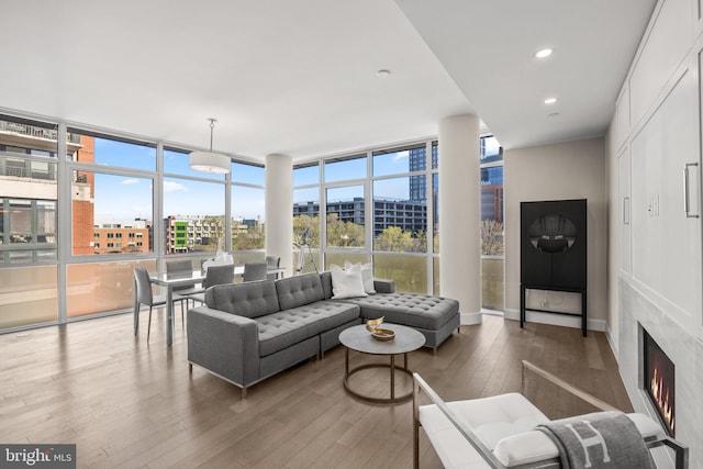 living area featuring expansive windows, a city view, a lit fireplace, and wood finished floors