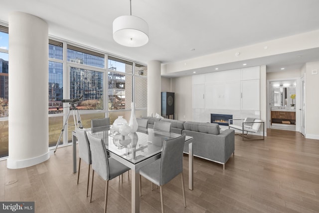 dining room featuring recessed lighting, wood finished floors, a lit fireplace, floor to ceiling windows, and a view of city