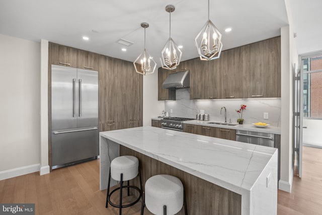 kitchen featuring premium appliances, under cabinet range hood, a sink, light wood-type flooring, and decorative light fixtures