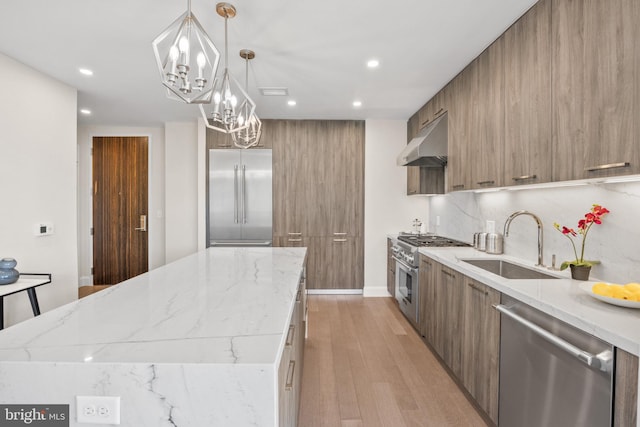 kitchen featuring high end appliances, modern cabinets, a sink, and under cabinet range hood