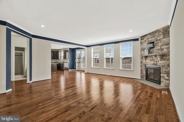 unfurnished living room with baseboards, wood finished floors, crown molding, a fireplace, and recessed lighting