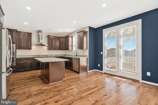 kitchen with stainless steel appliances, dark brown cabinets, wall chimney range hood, light wood-type flooring, and a center island