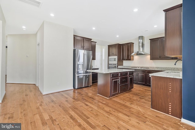 kitchen featuring stainless steel appliances, a sink, visible vents, a center island, and wall chimney exhaust hood